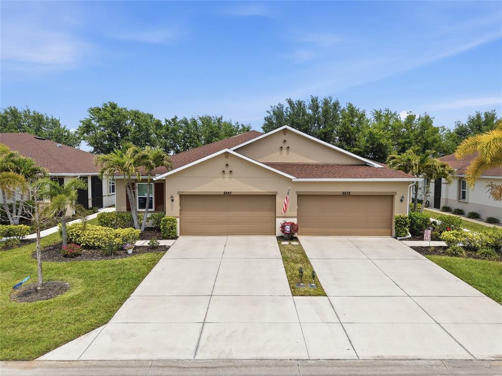 A tan duplex home features two garage doors and a concrete driveway under a blue sky — 8834 TUSCANY ISLES DRIVE, PUNTA GORDA, FL