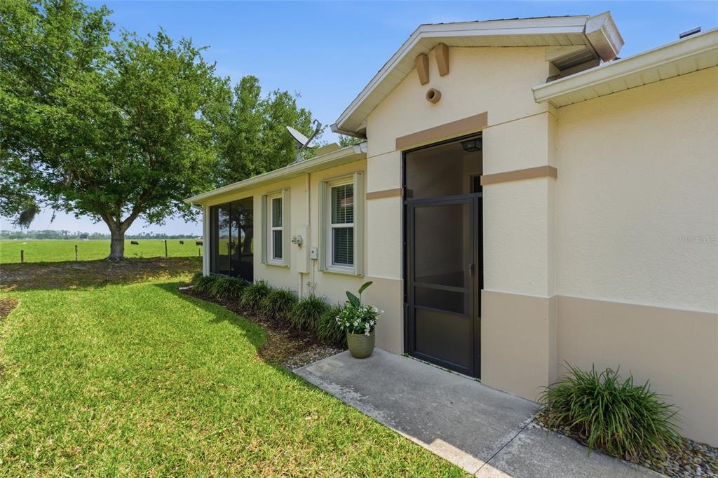 A side view of a house exterior with a screened door and a grassy yard — 8834 TUSCANY ISLES DRIVE, PUNTA GORDA, FL