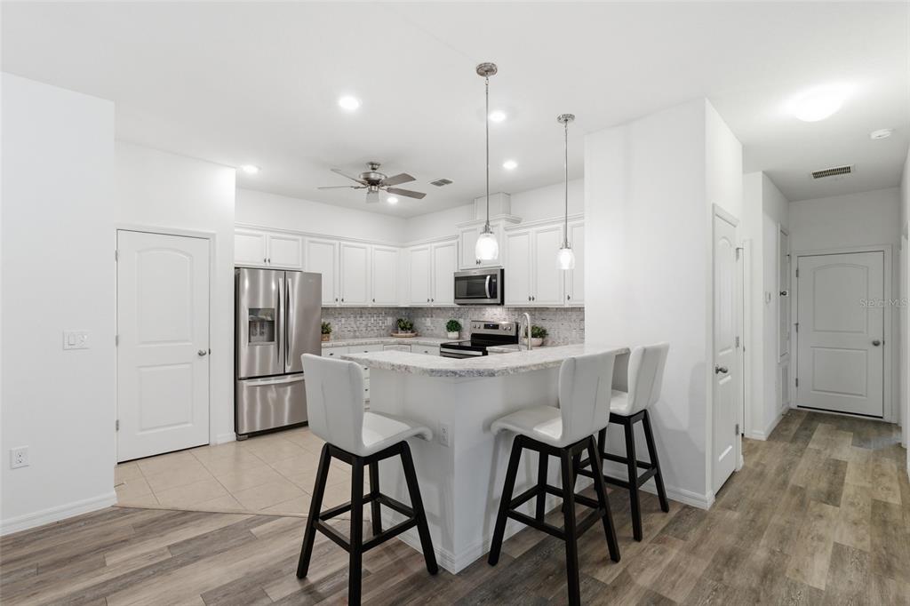 A modern kitchen features white cabinetry, stainless steel appliances, a breakfast bar, and wood-look flooring — 8834 TUSCANY ISLES DRIVE, PUNTA GORDA, FL
