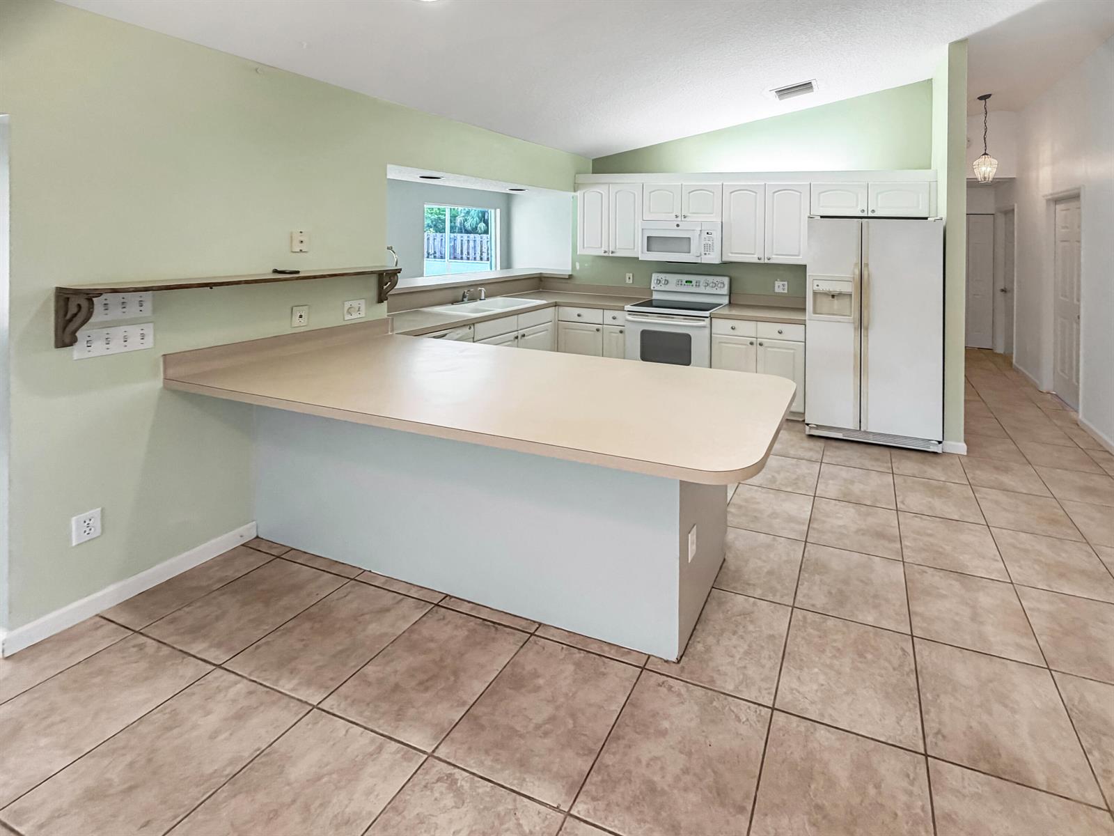 A kitchen features white cabinets, beige countertops, tile flooring, and a breakfast bar peninsula — 2361 NE 21st Avenue, Jensen Beach FL 34957, JENSEN BEACH, FL
