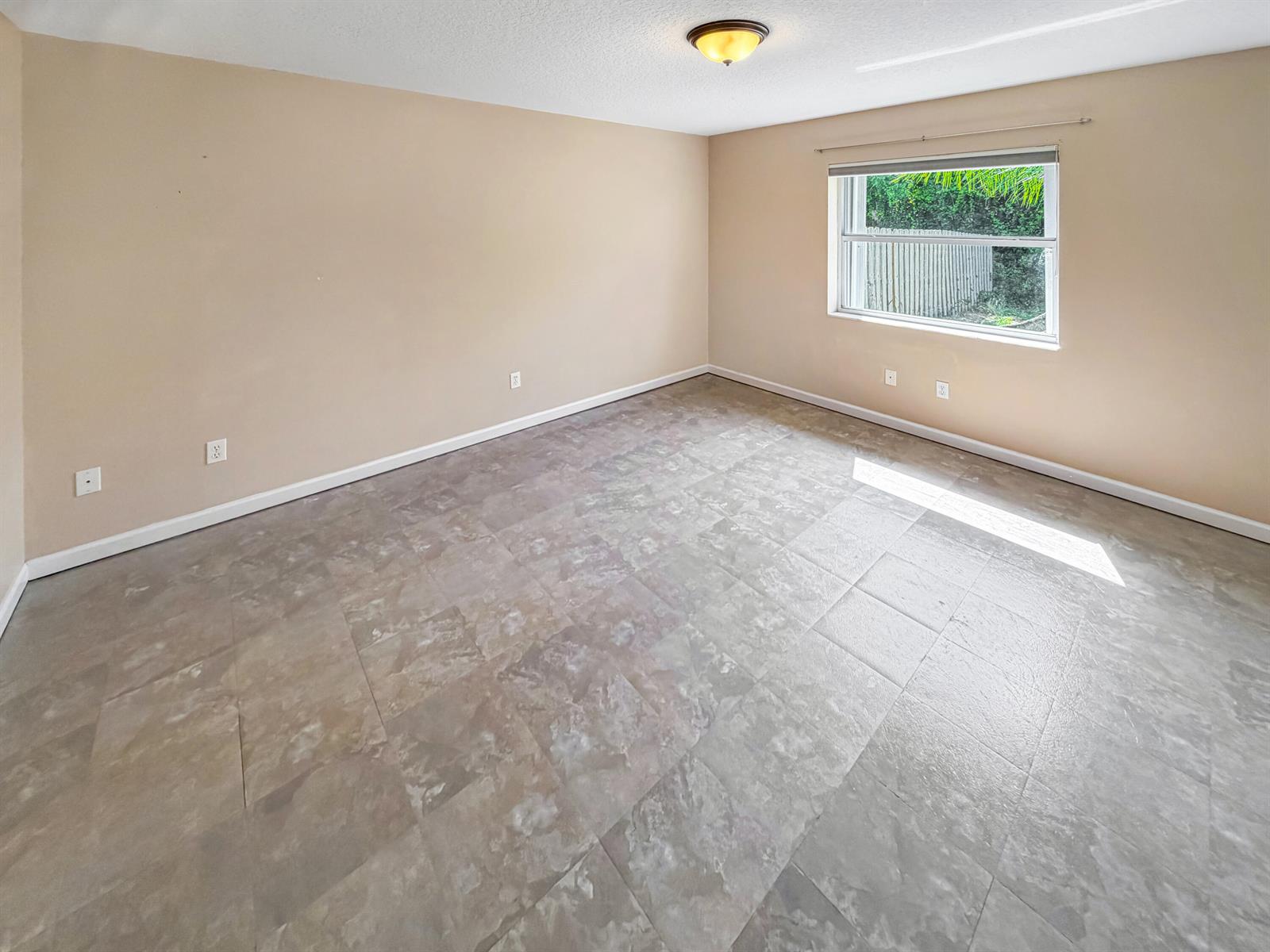 An empty bedroom features beige walls, a single window, and gray square tile flooring — 2361 NE 21st Avenue, Jensen Beach FL 34957, JENSEN BEACH, FL