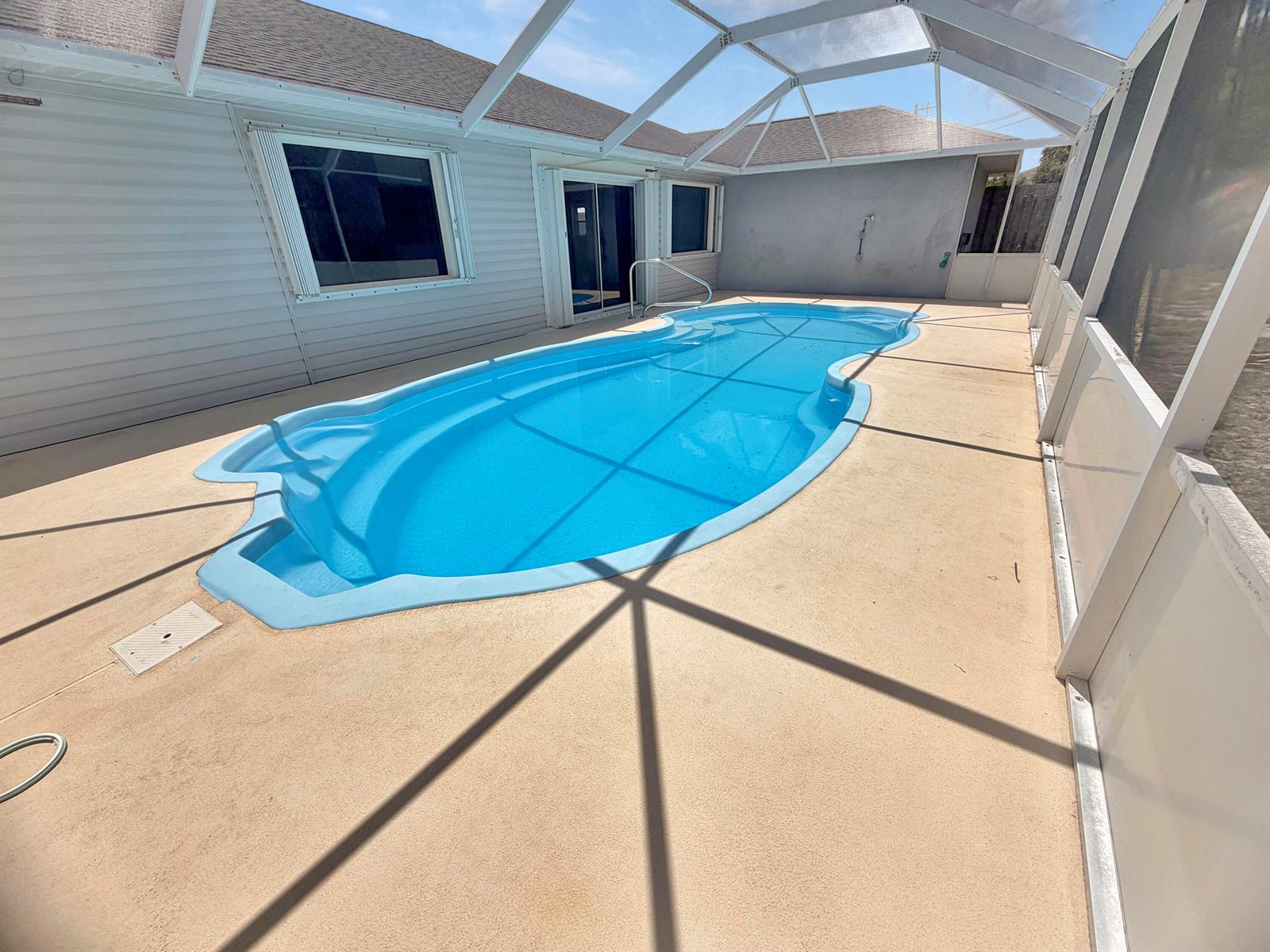 A swimming pool with a screened-in enclosure sits on a concrete patio beside a house — 2361 NE 21st Avenue, Jensen Beach FL 34957, JENSEN BEACH, FL