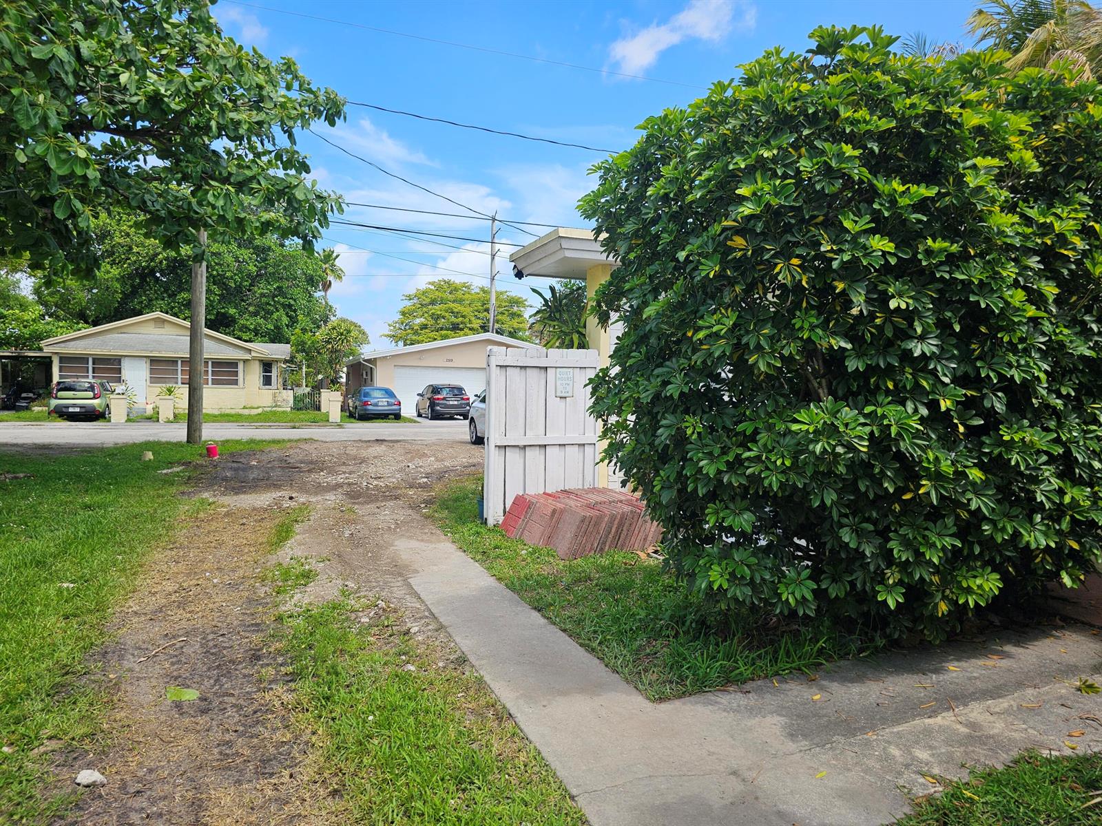 A view of a residential street with a dirt driveway, a white fence, and landscaping — 2512 Arthur Street, Hollywood FL 33020, HOLLYWOOD, FL