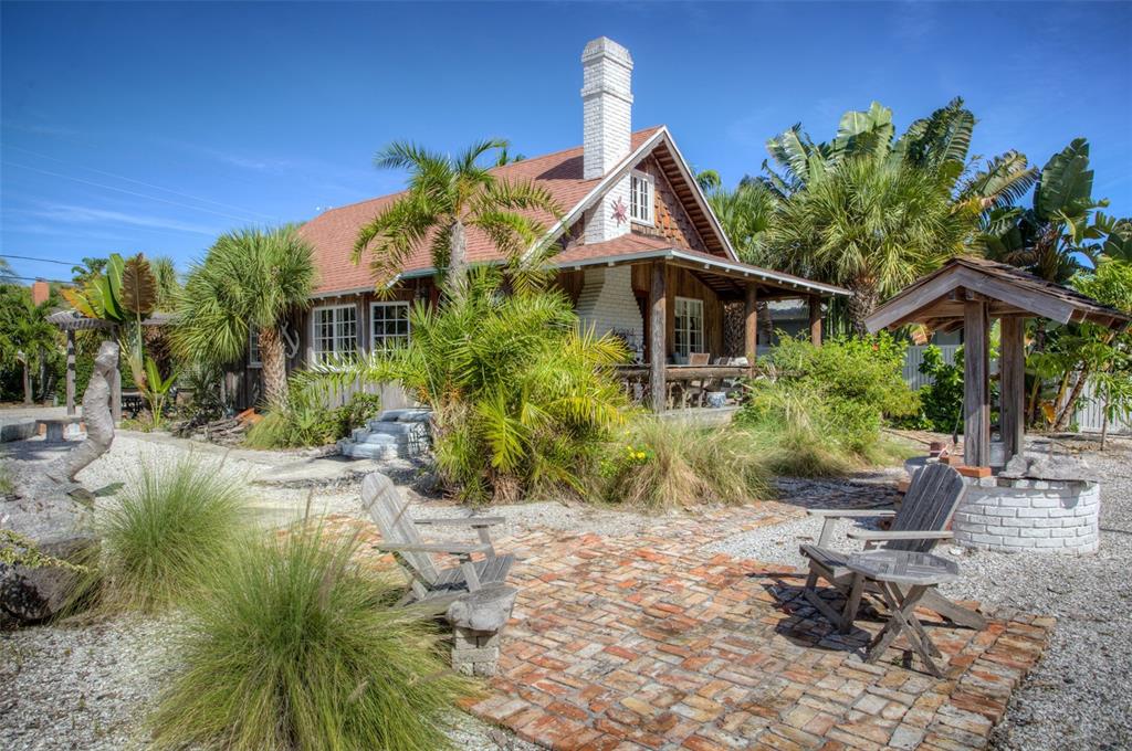 A rustic wooden cottage with a white brick chimney sits behind a brick patio area — 3000 PASS A GRILLE WAY, ST PETE BEACH, FL