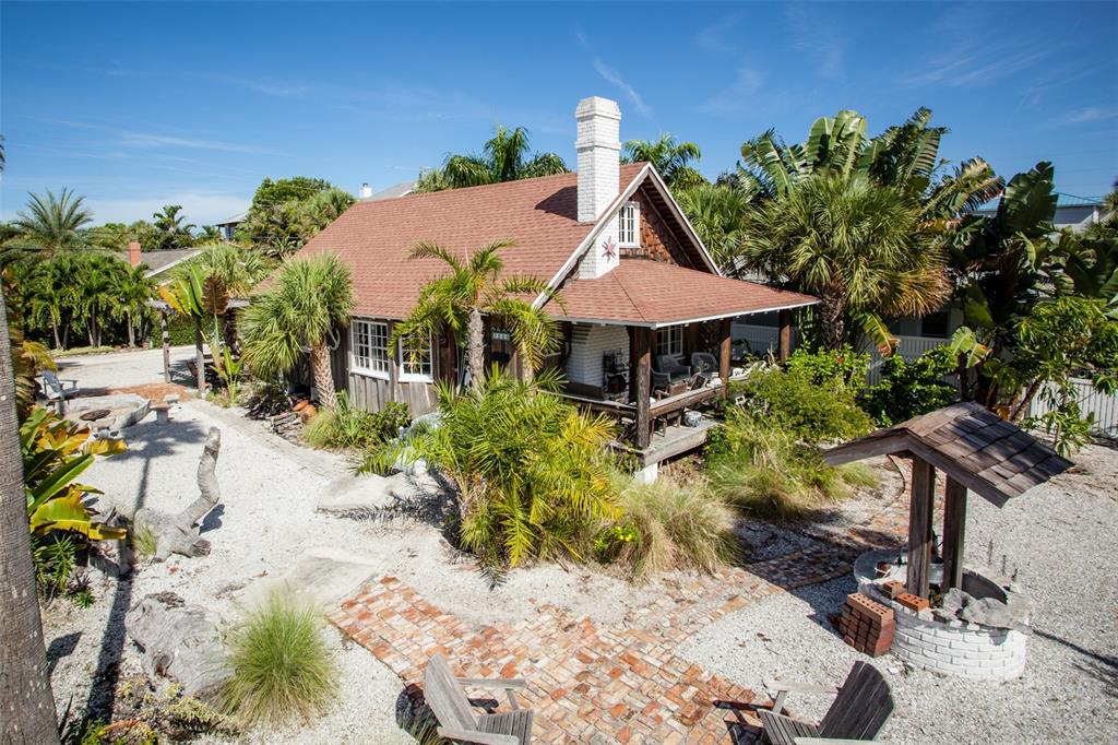 A rustic cottage with a brick chimney and a covered porch sits on a gravel lot — 3000 PASS A GRILLE WAY, ST PETE BEACH, FL