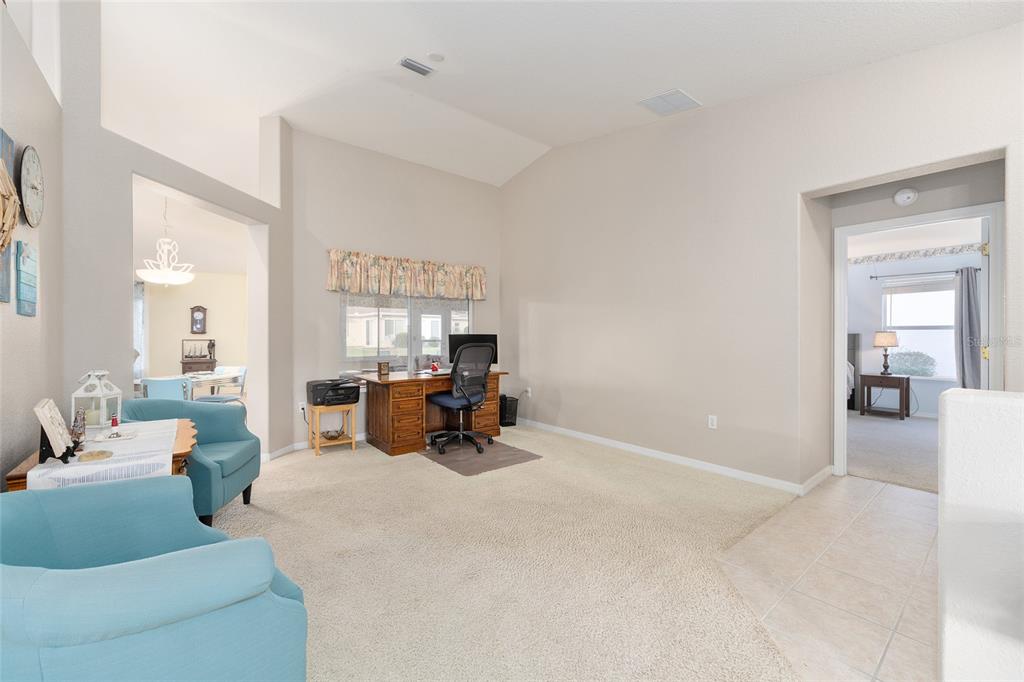 A carpeted room features a wooden desk, two blue armchairs, and a vaulted ceiling — 8789 SE 136TH LANE, SUMMERFIELD, FL
