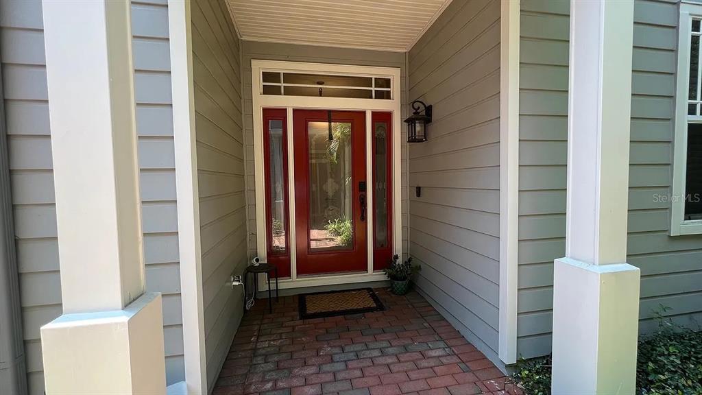 A red front door with glass panels sits under a covered porch with brick flooring — 2889 BAYSHORE TRAILS DRIVE, TAMPA, FL
