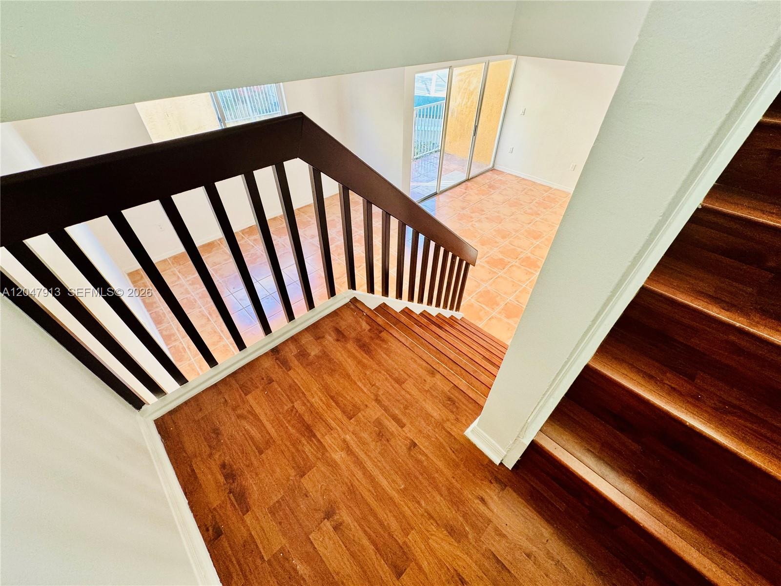 A wooden staircase with a dark railing overlooks a lower level with tiled flooring — 6245 Kendale Lakes Cir # 208, Miami FL 33183, MIAMI, FL