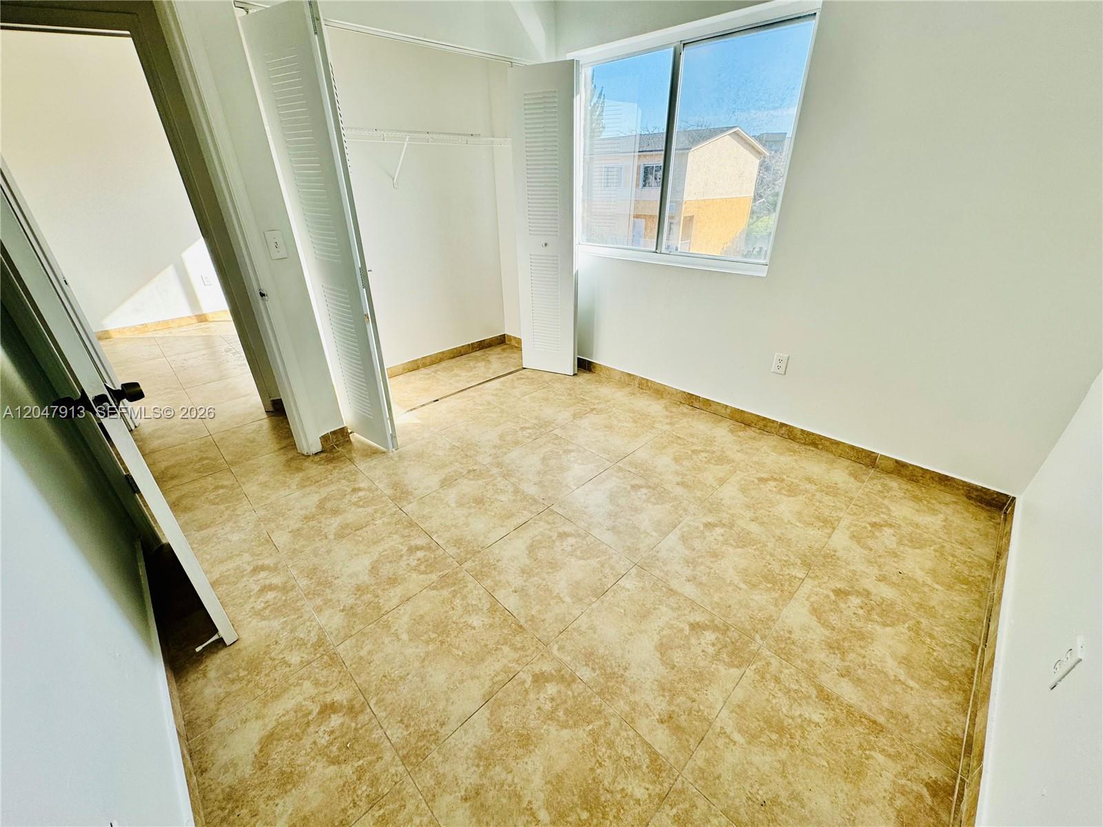 An empty bedroom features beige tile flooring, a white closet, and a large window — 6245 Kendale Lakes Cir # 208, Miami FL 33183, MIAMI, FL