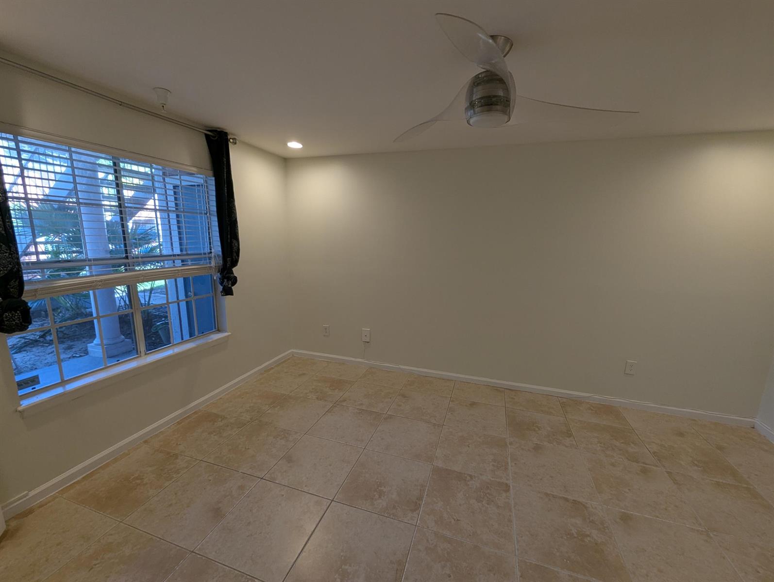 An empty room features beige tile flooring, a ceiling fan, and a large window — 1335 Crystal Way, Delray Beach FL 33444, DELRAY BEACH, FL