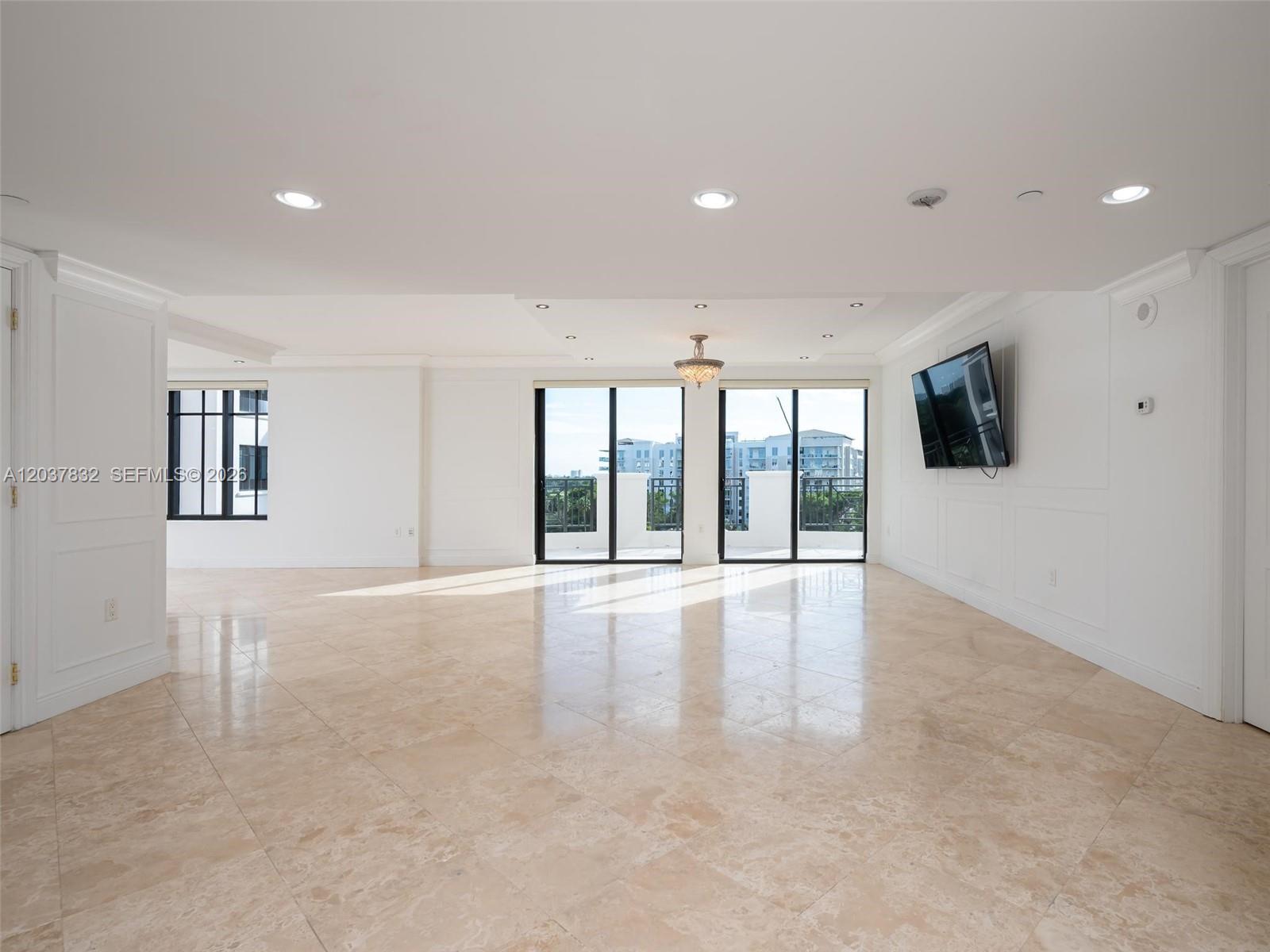 A spacious, bright living room features light-colored tile flooring, white walls, and large glass doors — 200 E Palmetto Park Rd # 700, Boca Raton FL 33432, BOCA RATON, FL