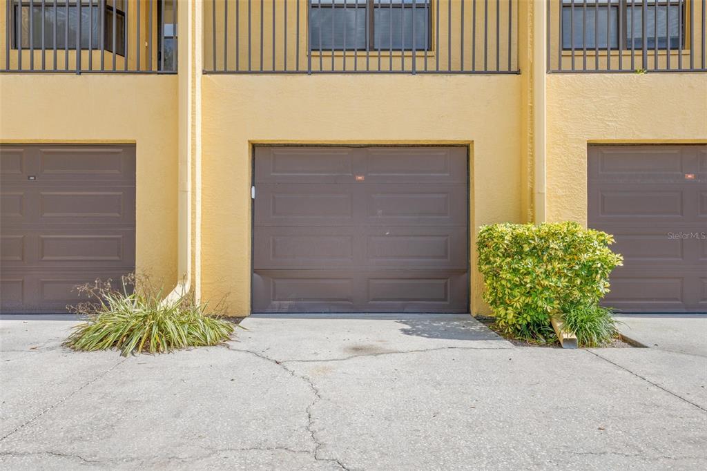 A row of three brown garage doors set into a yellow stucco building exterior — 5817 PARK STREET N UNIT 302, ST PETERSBURG, FL