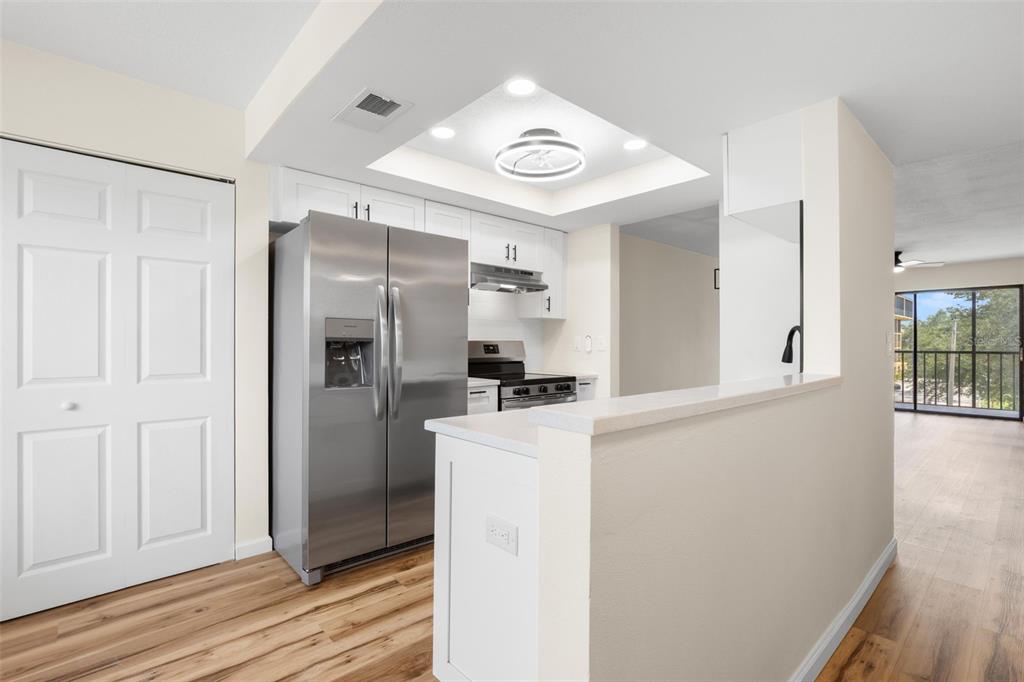 A kitchen with white cabinets, stainless steel appliances, and a breakfast bar overlooking a room — 5817 PARK STREET N UNIT 302, ST PETERSBURG, FL