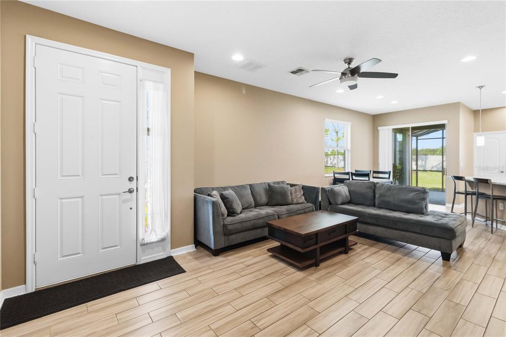 A living room with light wood-look tile flooring, gray sectional sofas, and a white front door — 2618 WHITE ISLE LANE, ORLANDO, FL
