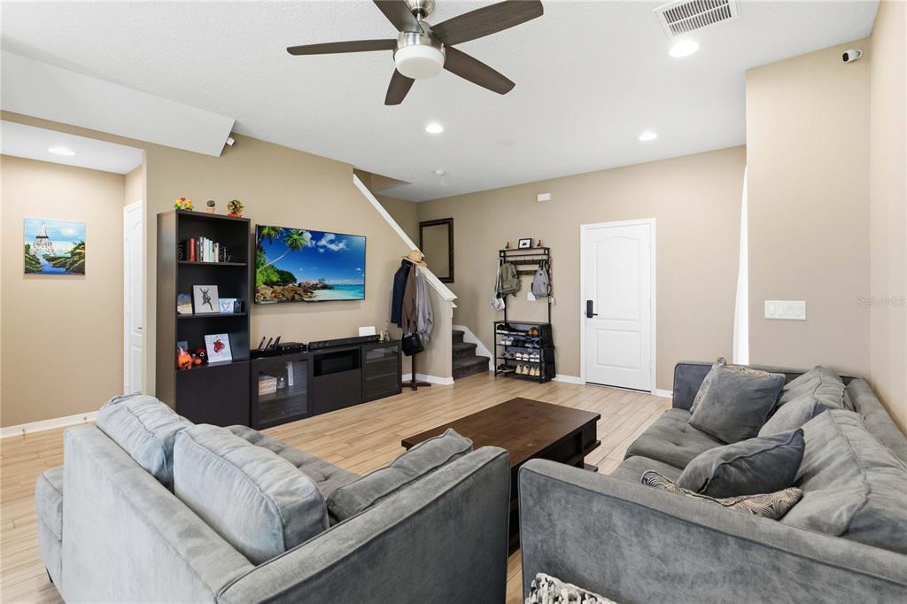 A living room features gray sectional sofas, a television, a bookshelf, and light wood flooring — 2618 WHITE ISLE LANE, ORLANDO, FL