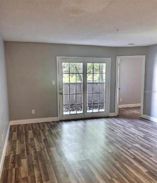 An interior room with gray walls, wood-look flooring, and glass French doors leading outside — 199 AFTON SQUARE UNIT 107, ALTAMONTE SPRINGS, FL