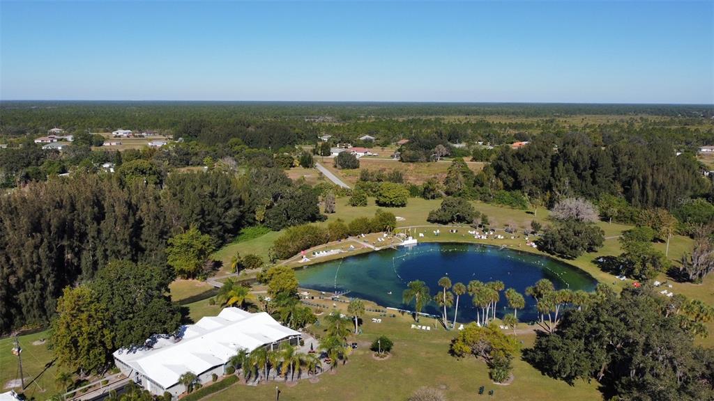An aerial view shows a swimming spring surrounded by trees, grass, and a white building — SARAGOSSA LANE, NORTH PORT, FL