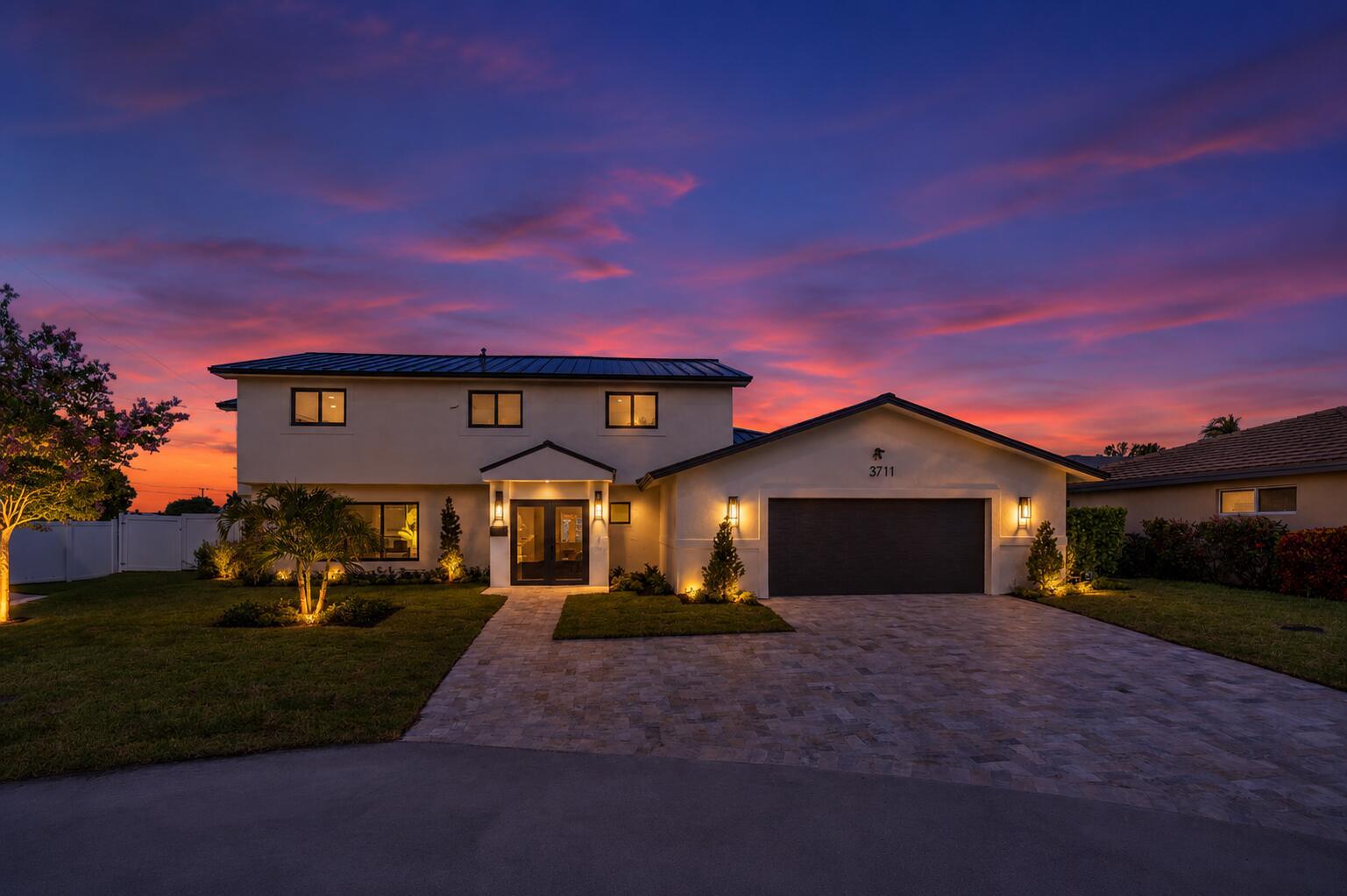 A two-story house with a paved driveway and landscape lighting at sunset — 3711 NE 27th Avenue, Lighthouse Point FL 33064, LIGHTHOUSE POINT, FL