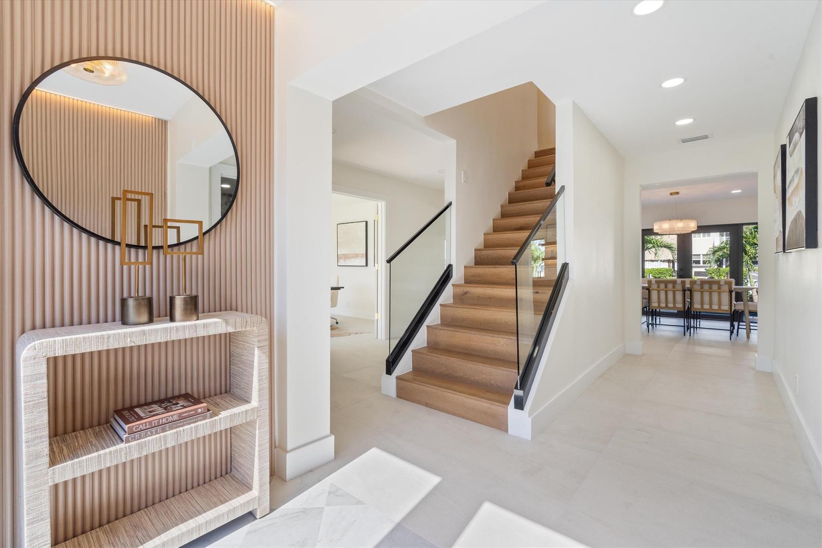 A modern entryway features a slatted wood wall, a circular mirror, and a wooden staircase — 3711 NE 27th Avenue, Lighthouse Point FL 33064, LIGHTHOUSE POINT, FL