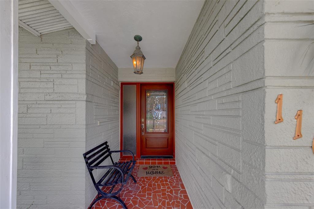 A covered entryway features a red front door, a black bench, and textured stone walls — 11602 GROVE STREET, SEMINOLE, FL