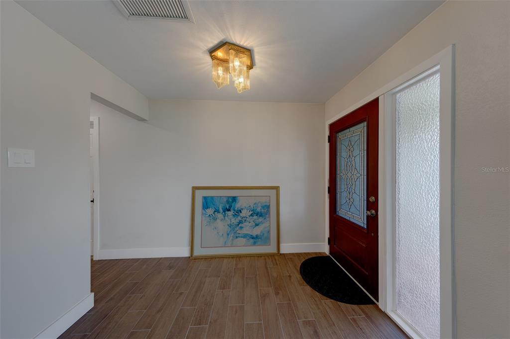 An entryway features wood-look tile flooring, a red front door with glass, and a crystal light — 11602 GROVE STREET, SEMINOLE, FL
