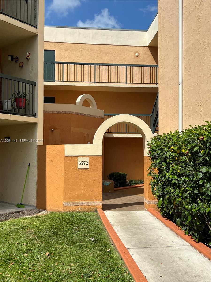An exterior view of a two-story apartment building with a central arched entryway — 6272 NW 186th St # 104, Hialeah FL 33015, HIALEAH, FL