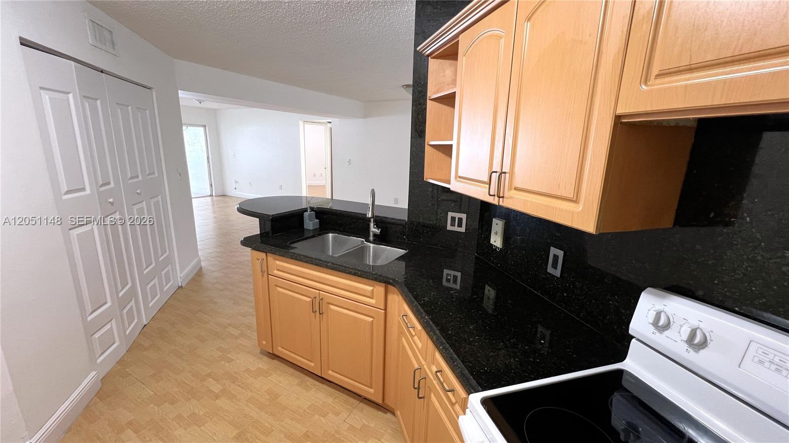A kitchen features light wood cabinets, black granite countertops, and a double-basin sink — 6272 NW 186th St # 104, Hialeah FL 33015, HIALEAH, FL