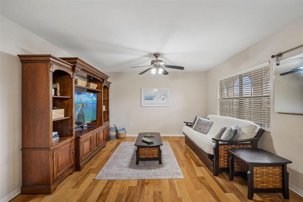A living room features a large wooden entertainment center, a futon, and hardwood flooring — 6100 GULFPORT BOULEVARD S UNIT 402, GULFPORT, FL