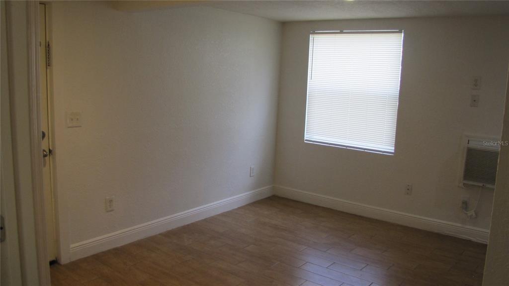 An empty room features light-colored walls, wood-look tile flooring, a window with blinds, and an AC unit — 109 E GLADYS STREET UNIT D, TAMPA, FL