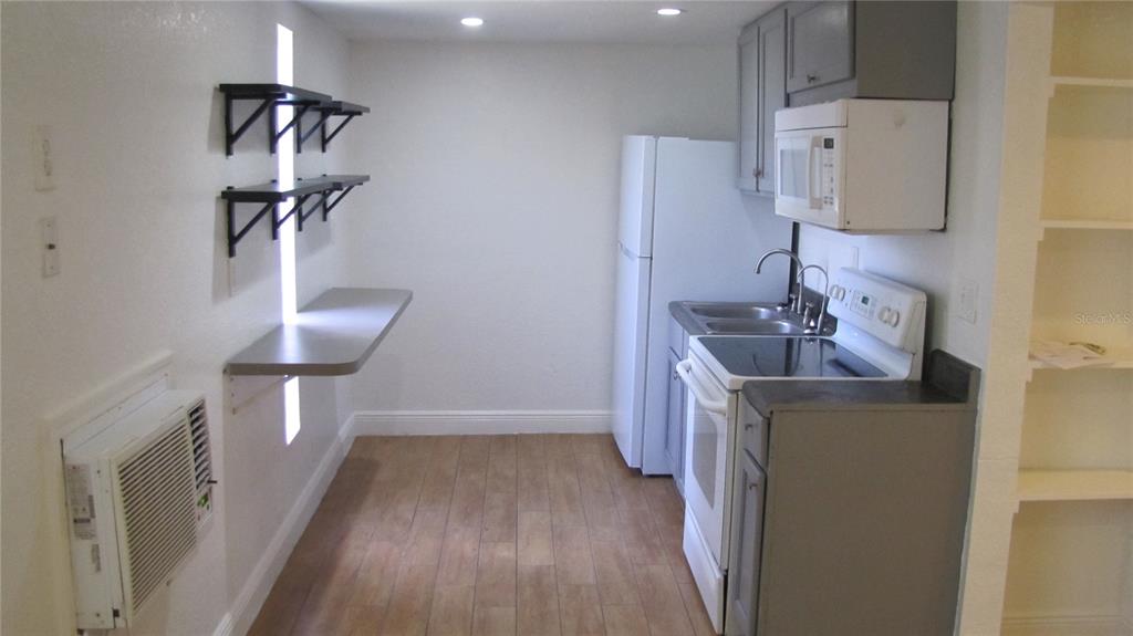 A small kitchen features white appliances, gray cabinets, wood-look flooring, and a wall-mounted desk area — 109 E GLADYS STREET UNIT D, TAMPA, FL