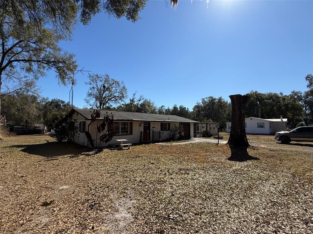 A single-story house with a large yard and a prominent tree stump in the foreground — 4404 ARECA PALM DRIVE, ZEPHYRHILLS, FL