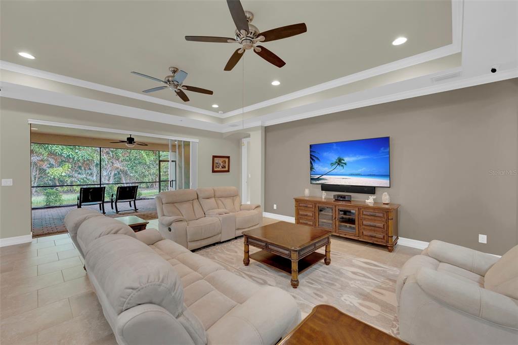 A living room features a tray ceiling, two ceiling fans, beige sofas, and a television — 8720 WESTWOOD OAKS PLACE, FORT MYERS, FL