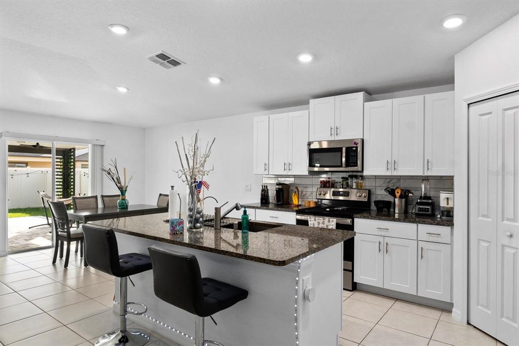 A kitchen with white cabinets, granite countertops, a center island, and a dining area — 32024 HAWTHORNE COTTAGE PLACE, SAN ANTONIO, FL
