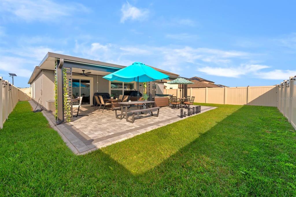 A backyard patio with a dining set, umbrella, and vinyl fencing under a blue sky — 32024 HAWTHORNE COTTAGE PLACE, SAN ANTONIO, FL