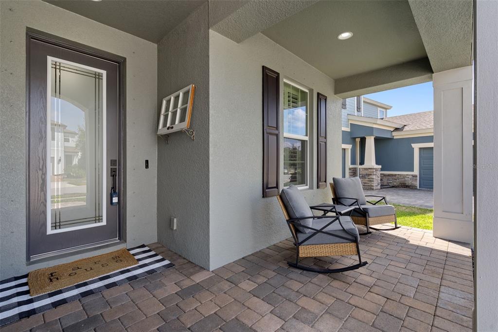 A covered front porch features gray stucco walls, a paved floor, and two rocking chairs — 18207 RAMBLE ON WAY, LAND O LAKES, FL