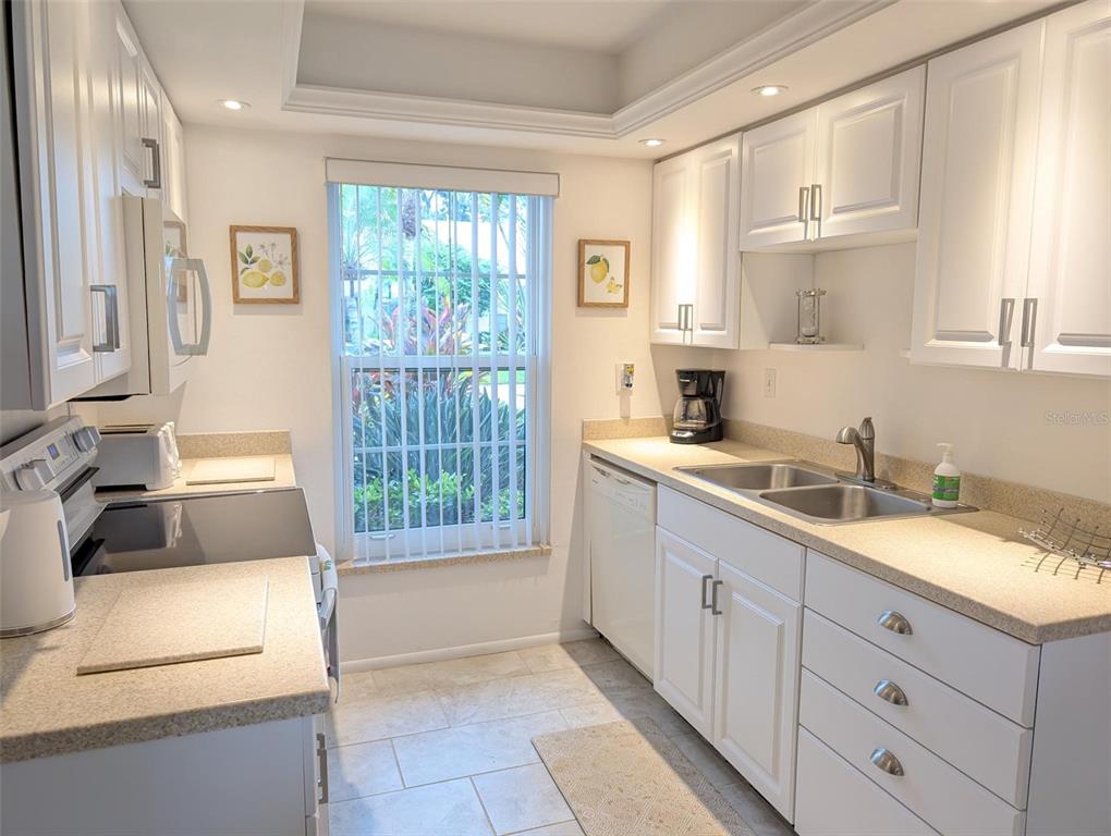 A bright kitchen features white cabinets, light countertops, a double sink, and a window view — 5377 CRESTLAKE BOULEVARD UNIT 69, SARASOTA, FL