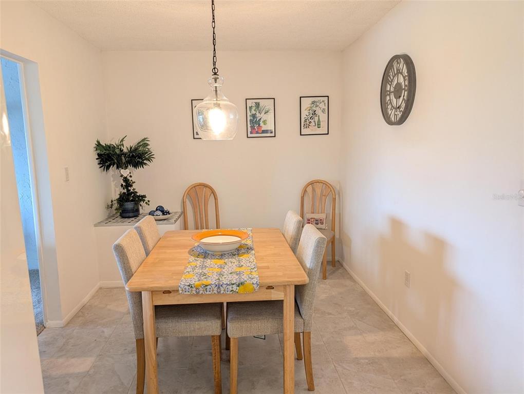 A dining room features a wooden table with upholstered chairs, a pendant light, and wall art — 5377 CRESTLAKE BOULEVARD UNIT 69, SARASOTA, FL