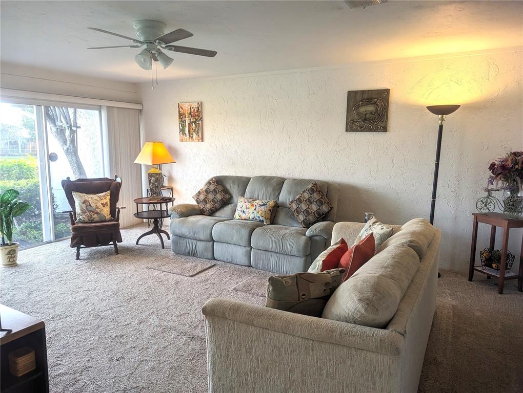 A living room features two sofas, an armchair, a floor lamp, and a sliding glass door — 5377 CRESTLAKE BOULEVARD UNIT 69, SARASOTA, FL