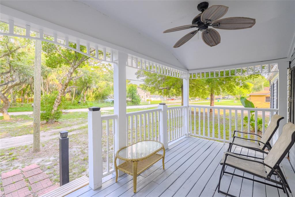 A covered porch features a ceiling fan, white railings, a small wicker table, and two chairs — 1419 OSCEOLA HOLLOW ROAD, ODESSA, FL