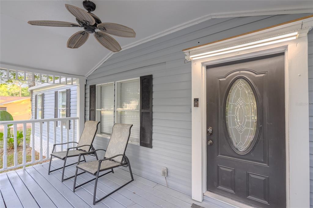 A covered front porch features gray siding, two chairs, a ceiling fan, and a dark door — 1419 OSCEOLA HOLLOW ROAD, ODESSA, FL