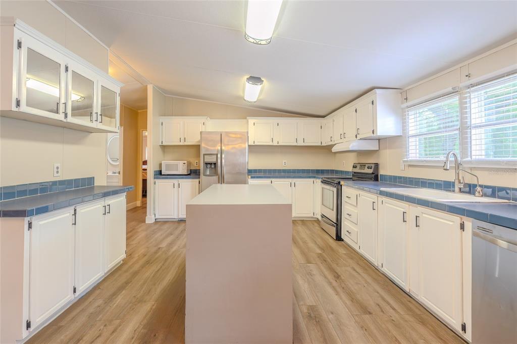 A kitchen features white cabinets, blue tile countertops, a center island, and wood-look flooring — 1419 OSCEOLA HOLLOW ROAD, ODESSA, FL
