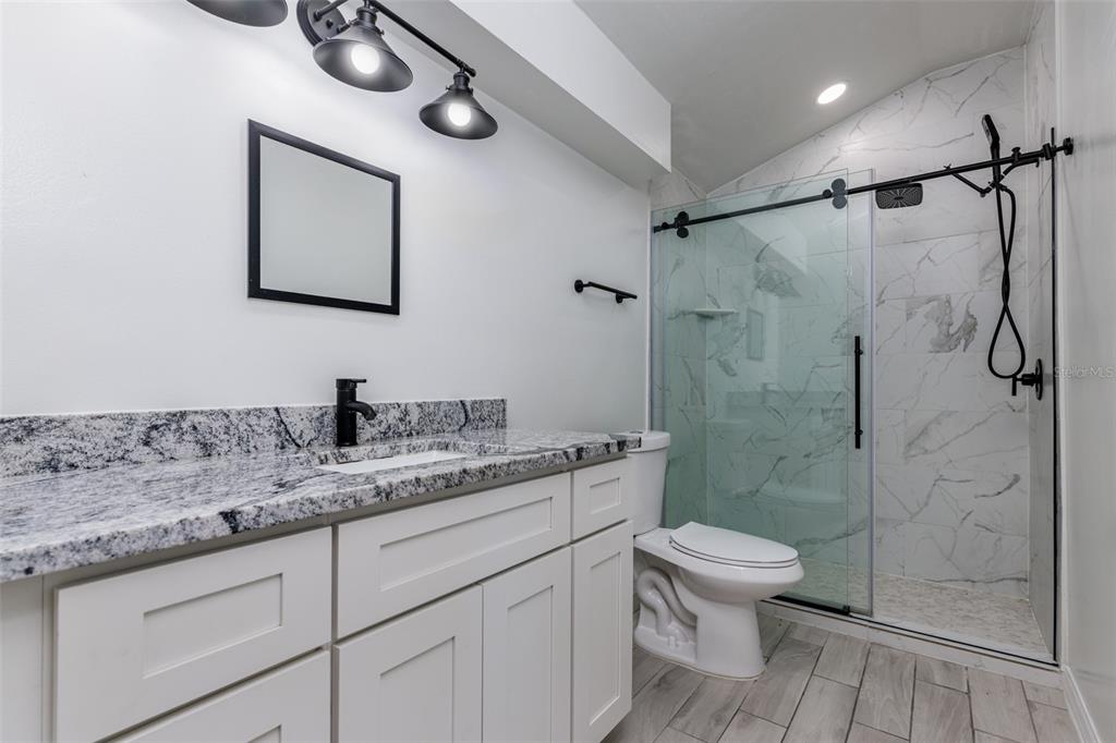 A modern bathroom features a white vanity with granite countertops, a toilet, and a glass-enclosed shower — 1177 NW 102ND BOULEVARD, WILDWOOD, FL