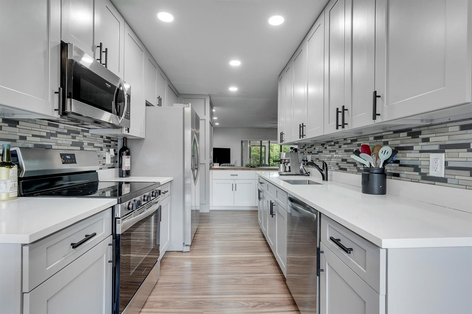 A galley kitchen features gray cabinets, white countertops, stainless steel appliances, and a tiled backsplash — 21691 Cypress Road # 16c, Boca Raton FL 33433, BOCA RATON, FL