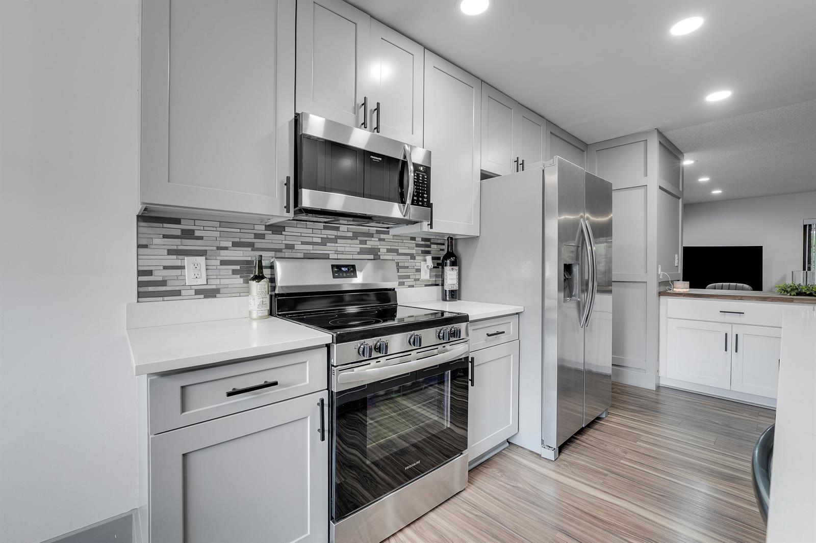 A kitchen features light gray cabinets, stainless steel appliances, white countertops, and a tiled backsplash — 21691 Cypress Road # 16c, Boca Raton FL 33433, BOCA RATON, FL