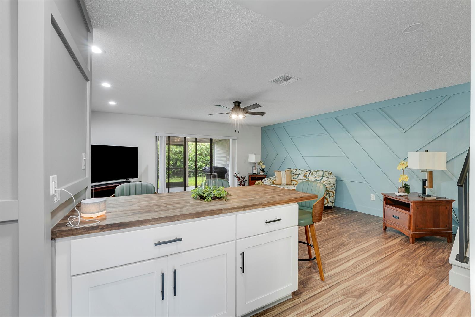 A kitchen island with a wood countertop faces a living area featuring a blue accent wall — 21691 Cypress Road # 16c, Boca Raton FL 33433, BOCA RATON, FL