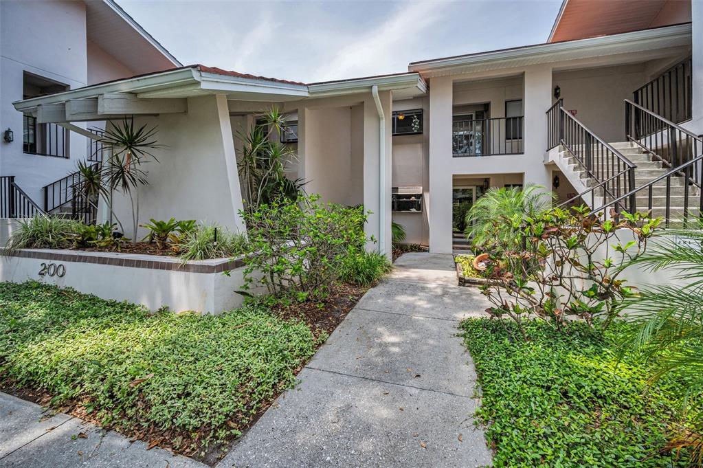 A concrete walkway leads to the entrance of a two-story apartment building with exterior stairs — 300 S FLORIDA AVENUE UNIT 200J, TARPON SPRINGS, FL