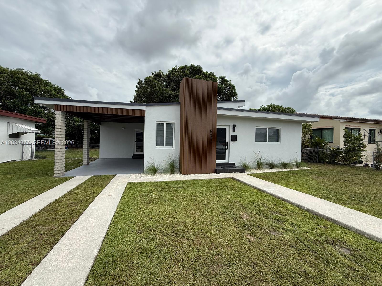 A single-story house features a white exterior, a wood-slat accent wall, and a covered carport — 521 E 33rd St, Hialeah FL 33013, HIALEAH, FL