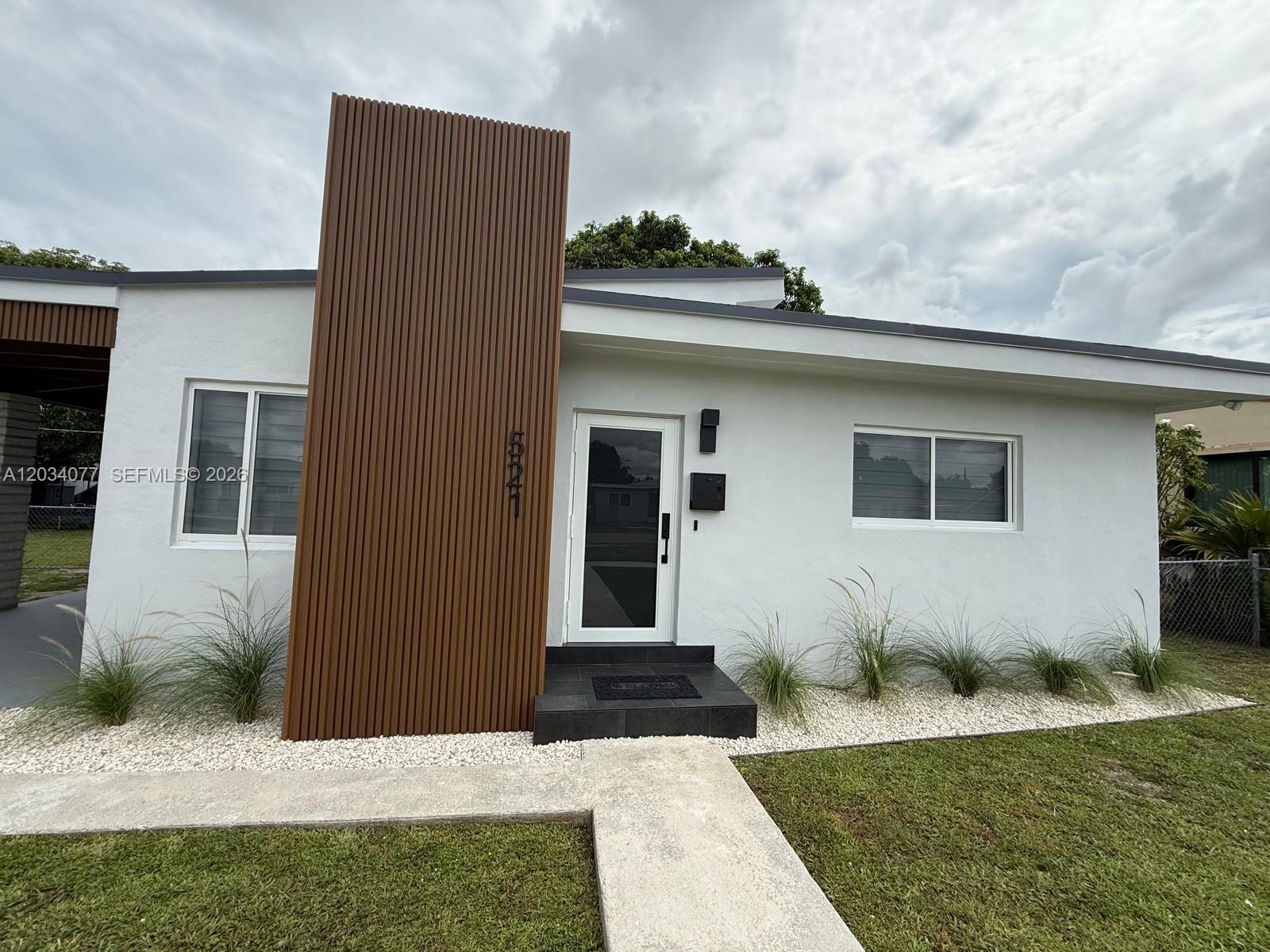The exterior of a white house features a prominent vertical wood-slat accent wall — 521 E 33rd St, Hialeah FL 33013, HIALEAH, FL