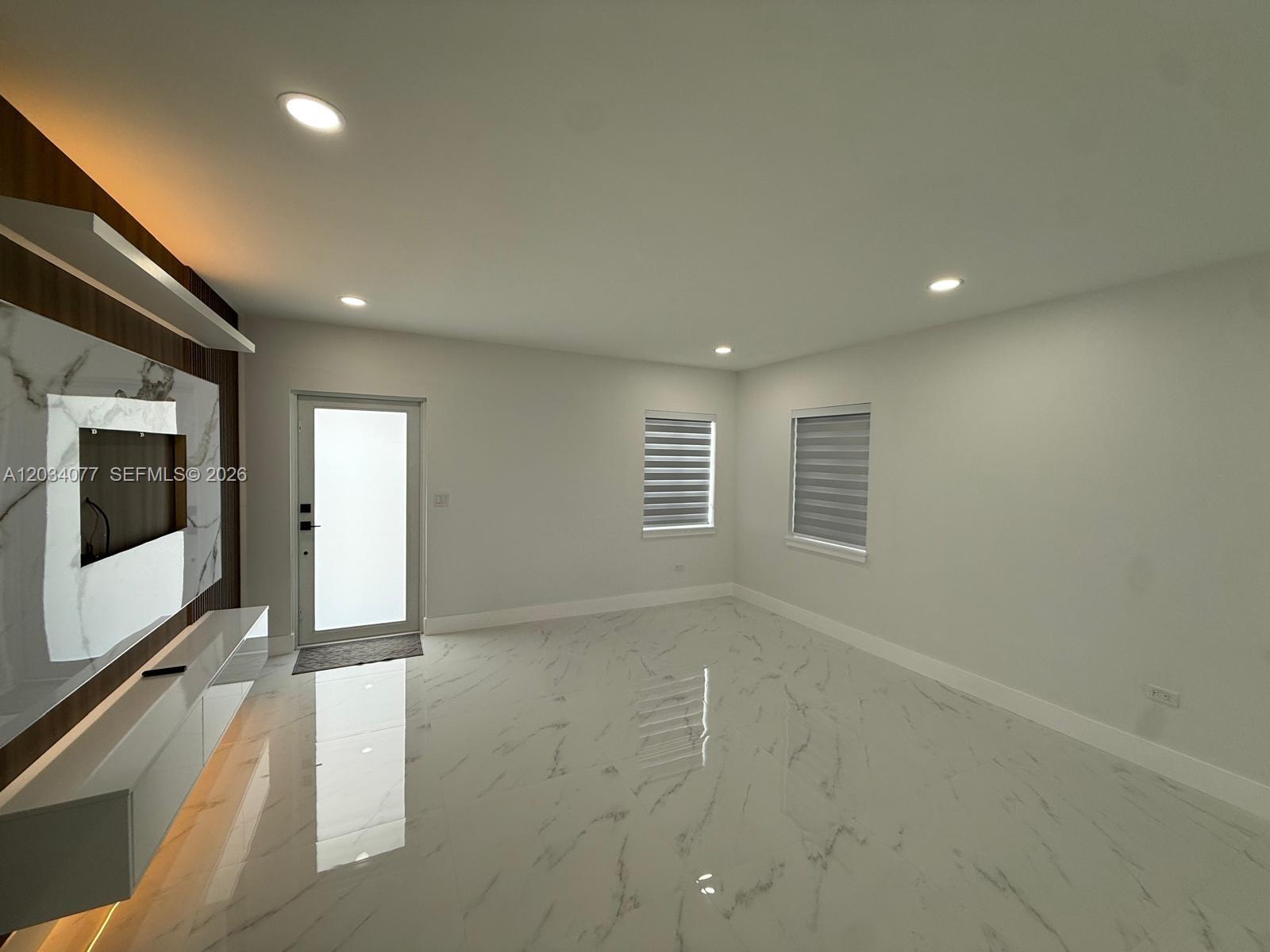 A modern living room features white marble floors, recessed lighting, and a wood-paneled media wall — 521 E 33rd St, Hialeah FL 33013, HIALEAH, FL
