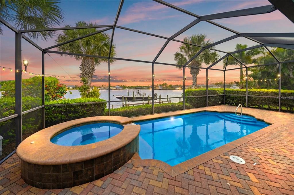 A screened-in pool and hot tub overlook a canal with a docked boat at sunset — 5040 LAKE OVERLOOK AVENUE, BRADENTON, FL